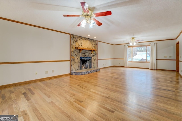 unfurnished living room featuring crown molding, a ceiling fan, a stone fireplace, wood finished floors, and baseboards