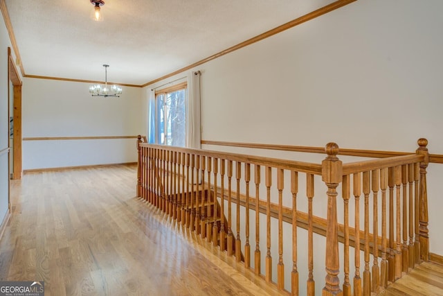 hall featuring baseboards, ornamental molding, wood finished floors, an inviting chandelier, and an upstairs landing