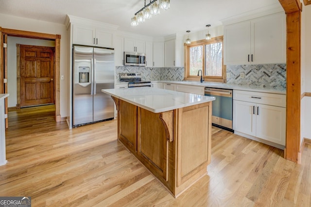 kitchen featuring white cabinets, a center island, stainless steel appliances, light wood-type flooring, and pendant lighting