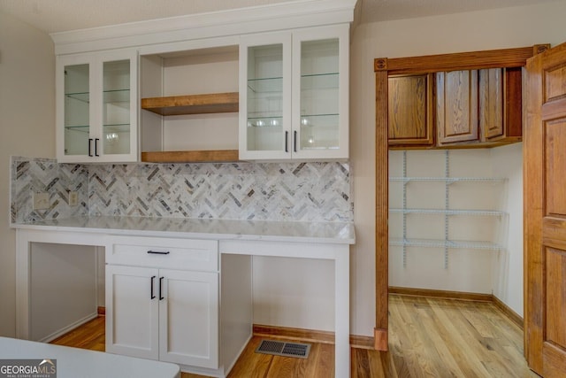 kitchen with glass insert cabinets, backsplash, white cabinets, and light wood-style floors