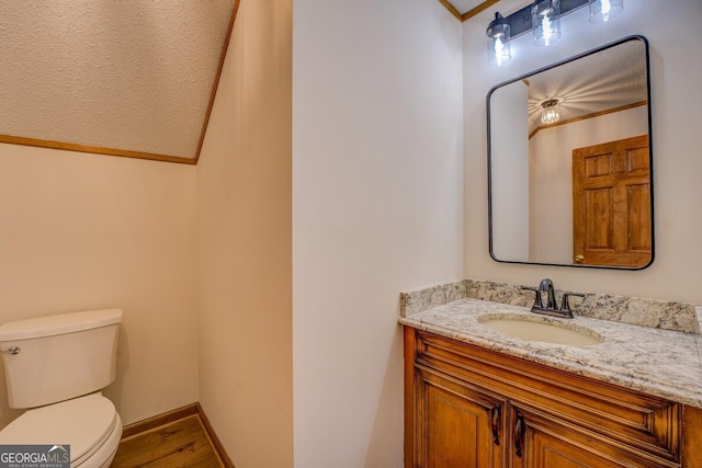 bathroom featuring toilet, wood finished floors, vanity, baseboards, and ornamental molding