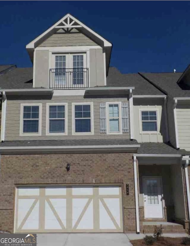 view of front of home featuring brick siding, an attached garage, and a balcony