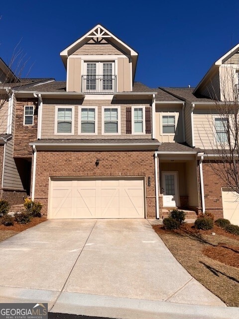 view of front of home featuring an attached garage, a balcony, concrete driveway, and brick siding