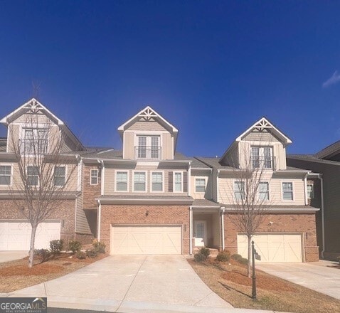 view of front of property with an attached garage, a balcony, concrete driveway, and brick siding