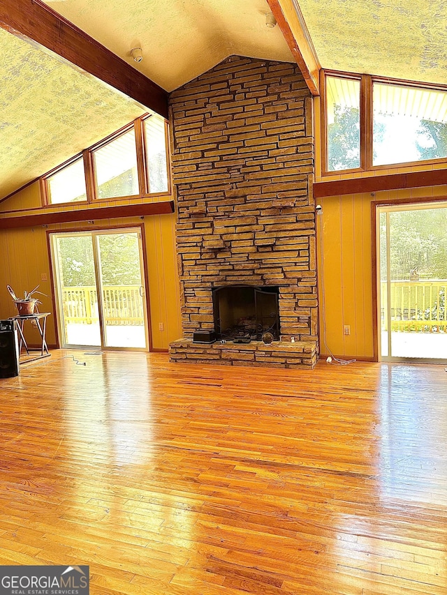 living room with beam ceiling, a fireplace, light wood-style floors, wood walls, and a textured ceiling