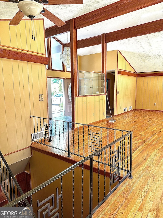 interior space with vaulted ceiling with beams, a ceiling fan, wood walls, a textured ceiling, and wood finished floors