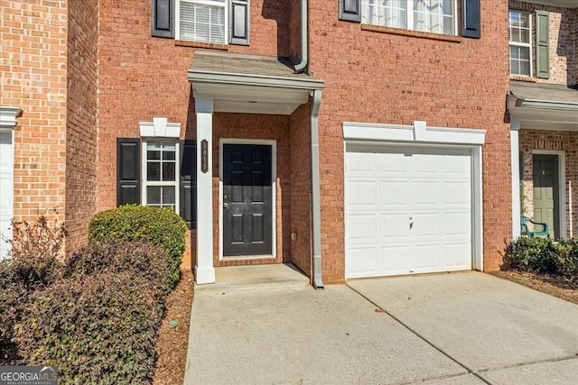 doorway to property featuring concrete driveway, brick siding, and an attached garage