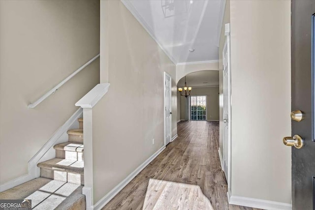 foyer entrance featuring arched walkways, baseboards, light wood-style floors, ornamental molding, and stairway