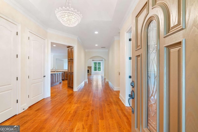 entryway featuring arched walkways, crown molding, wood finished floors, a chandelier, and baseboards