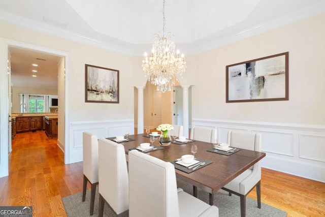 dining space with a wainscoted wall, ornamental molding, wood finished floors, and ornate columns