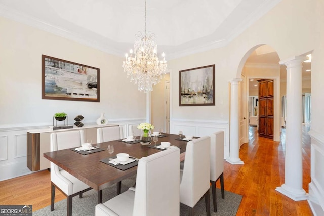 dining room featuring ornate columns, light wood-style flooring, arched walkways, and a decorative wall