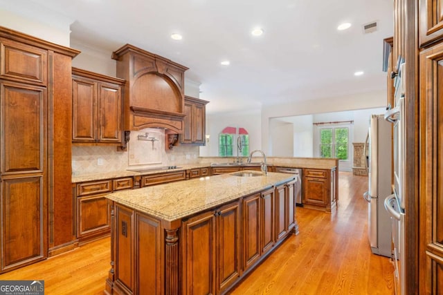 kitchen featuring stainless steel appliances, a sink, visible vents, brown cabinets, and a center island with sink