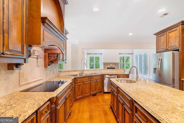 kitchen featuring light wood-type flooring, light stone countertops, appliances with stainless steel finishes, and a sink