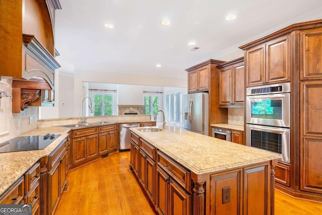 kitchen with a kitchen island with sink, light stone counters, stainless steel appliances, and a sink