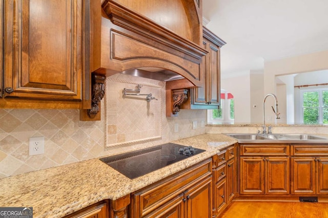 kitchen with light stone countertops, decorative backsplash, black electric cooktop, and a sink