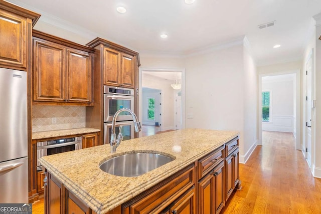 kitchen with a sink, a kitchen island, visible vents, appliances with stainless steel finishes, and brown cabinetry