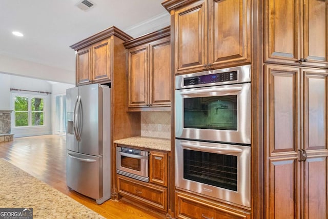 kitchen featuring light stone counters, visible vents, light wood-style floors, appliances with stainless steel finishes, and decorative backsplash