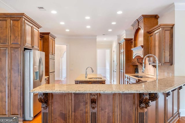 kitchen featuring a peninsula, stainless steel fridge, a sink, and light stone countertops