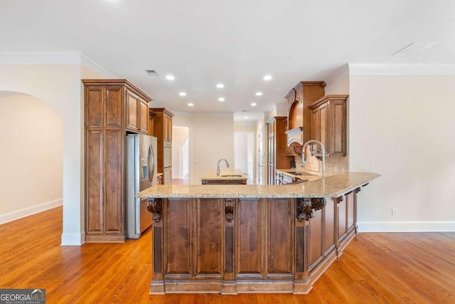 kitchen with light wood finished floors, light stone counters, brown cabinets, a peninsula, and stainless steel refrigerator with ice dispenser