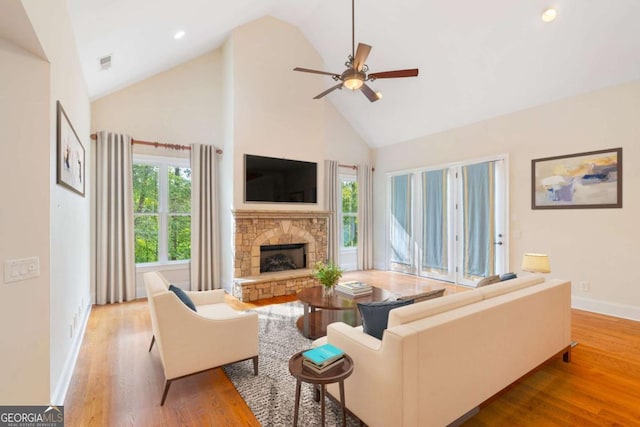 living area featuring a fireplace, visible vents, ceiling fan, high vaulted ceiling, and light wood-type flooring