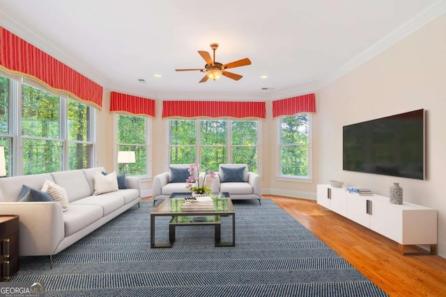 living area with a ceiling fan, ornamental molding, and wood finished floors