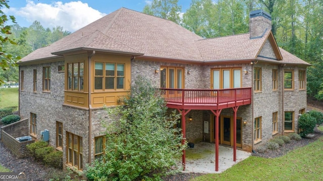 back of property with a wooden deck, a chimney, roof with shingles, a yard, and brick siding