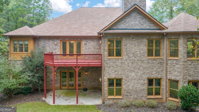 back of property featuring brick siding, a patio, a chimney, a shingled roof, and a deck