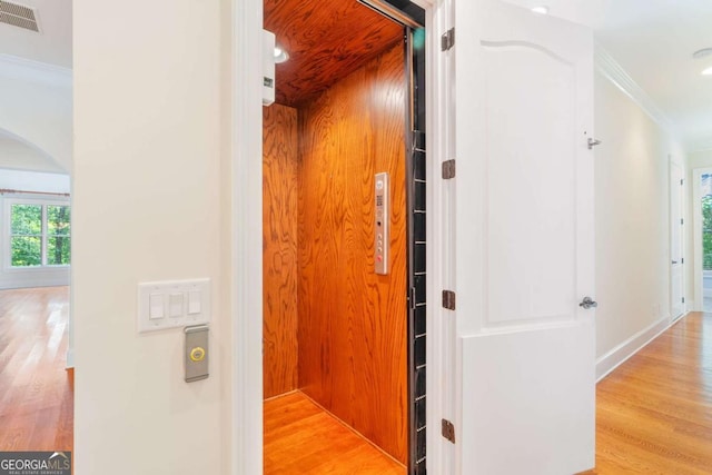 interior space featuring arched walkways, light wood finished floors, visible vents, ornamental molding, and elevator