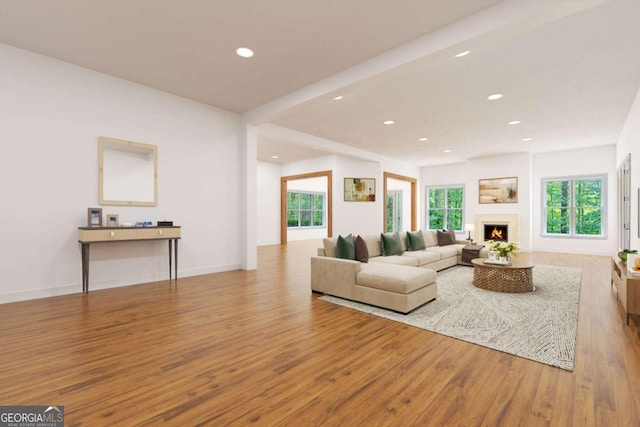 living room with recessed lighting, wood finished floors, a warm lit fireplace, beamed ceiling, and baseboards