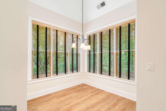 unfurnished dining area featuring a chandelier, wood finished floors, visible vents, and baseboards