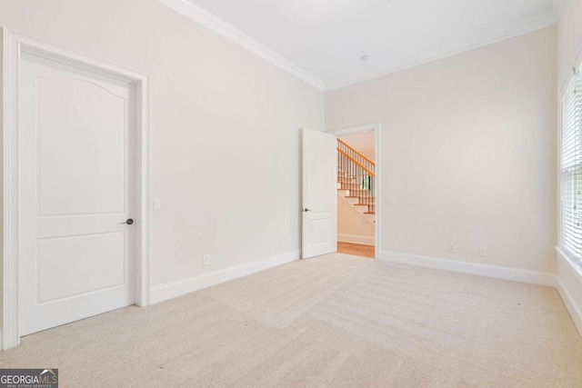 spare room featuring baseboards, ornamental molding, and light colored carpet