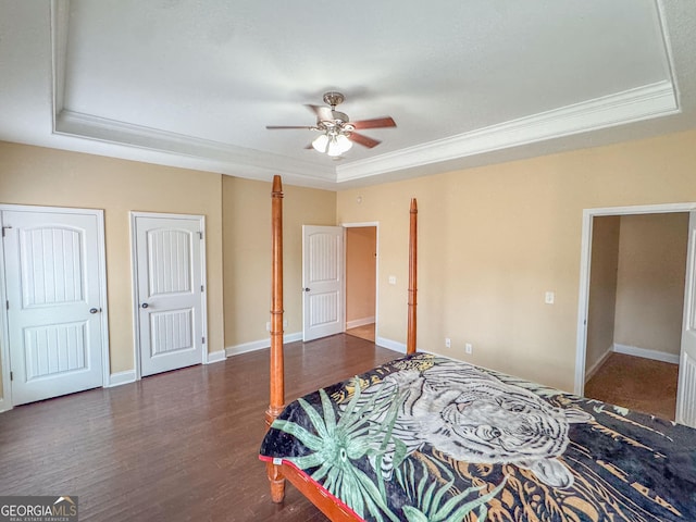 bedroom with baseboards, a raised ceiling, wood finished floors, crown molding, and two closets