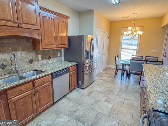 kitchen with brown cabinetry, hanging light fixtures, light stone countertops, stainless steel appliances, and a sink