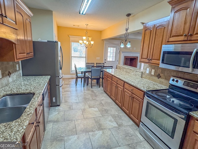 kitchen with light stone countertops, appliances with stainless steel finishes, brown cabinets, and decorative light fixtures