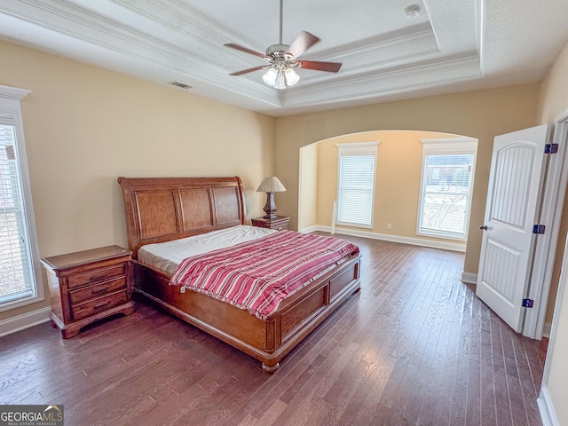 bedroom featuring a raised ceiling, multiple windows, crown molding, and dark wood-style flooring