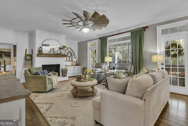 living area featuring a brick fireplace, wood finished floors, a ceiling fan, and ornamental molding