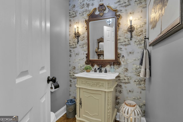 half bathroom featuring wallpapered walls, vanity, and baseboards