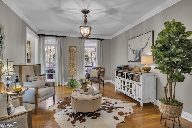 living area featuring crown molding, a notable chandelier, wood finished floors, and baseboards