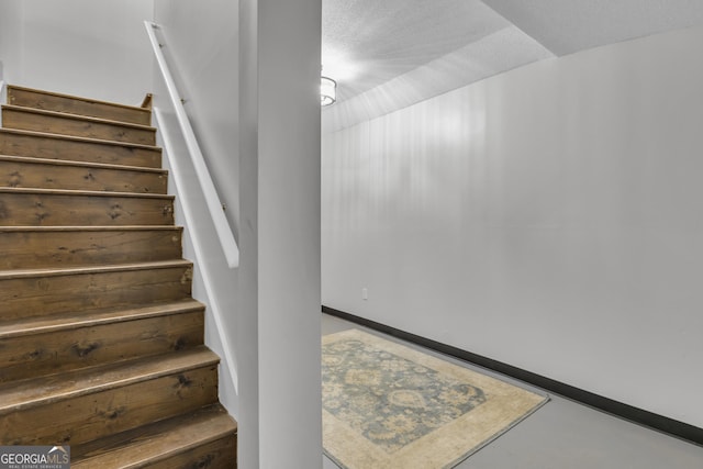 staircase featuring a textured ceiling, baseboards, and finished concrete floors