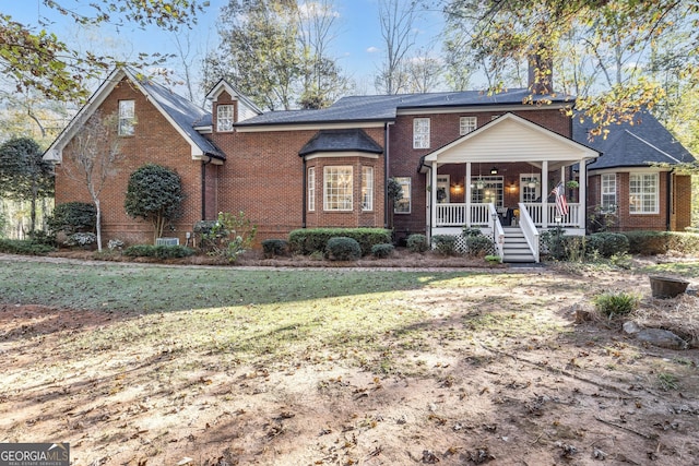 view of front facade with a porch, brick siding, a front yard, and a chimney