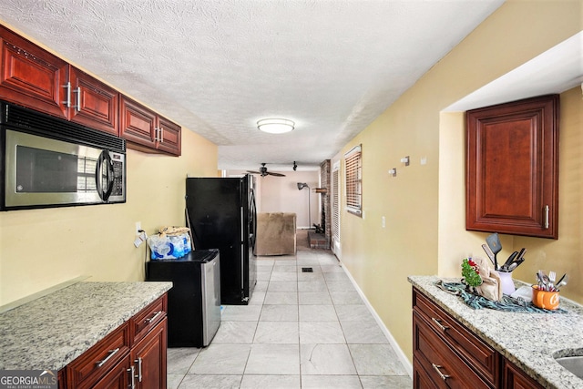 kitchen featuring a textured ceiling, light stone counters, baseboards, dark brown cabinets, and freestanding refrigerator