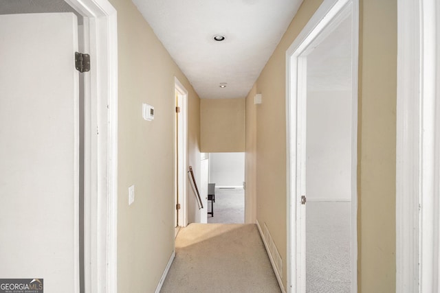 hallway featuring baseboards, carpet flooring, and an upstairs landing