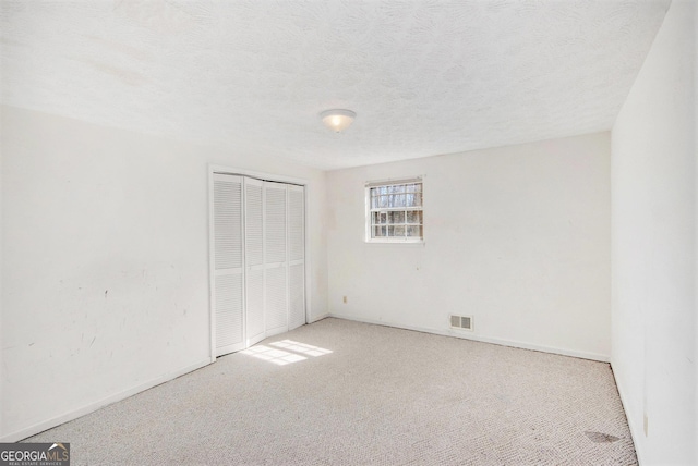 unfurnished bedroom with a textured ceiling, a closet, visible vents, and carpet flooring