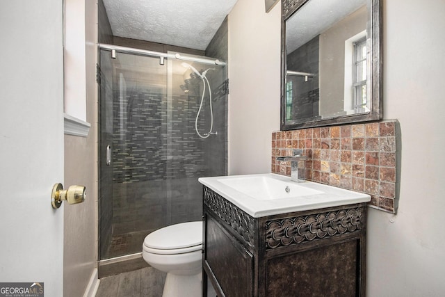 bathroom featuring decorative backsplash, toilet, a shower stall, a textured ceiling, and vanity