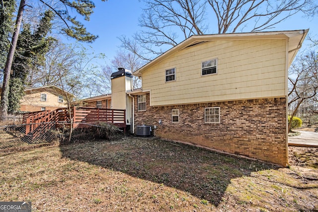 back of house with a chimney, fence, a deck, cooling unit, and brick siding