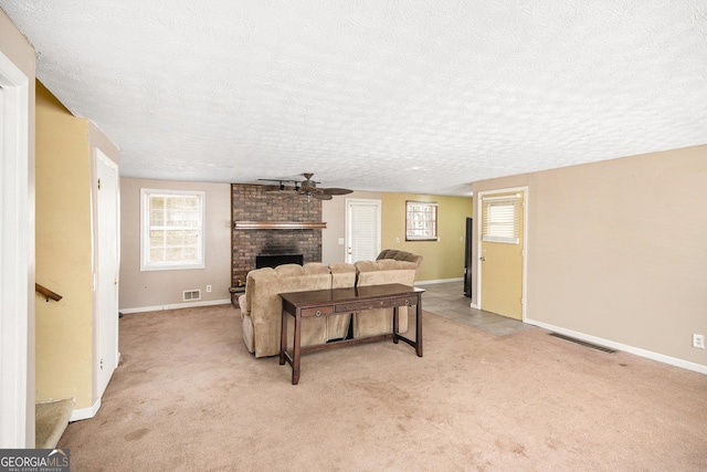 living area featuring light carpet, a textured ceiling, a brick fireplace, and visible vents