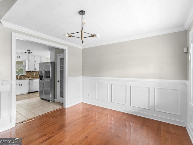 unfurnished dining area featuring light wood finished floors, visible vents, wainscoting, crown molding, and a notable chandelier