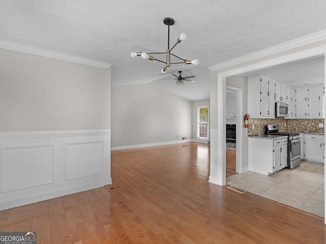 kitchen with light wood finished floors, white cabinets, appliances with stainless steel finishes, open floor plan, and pendant lighting