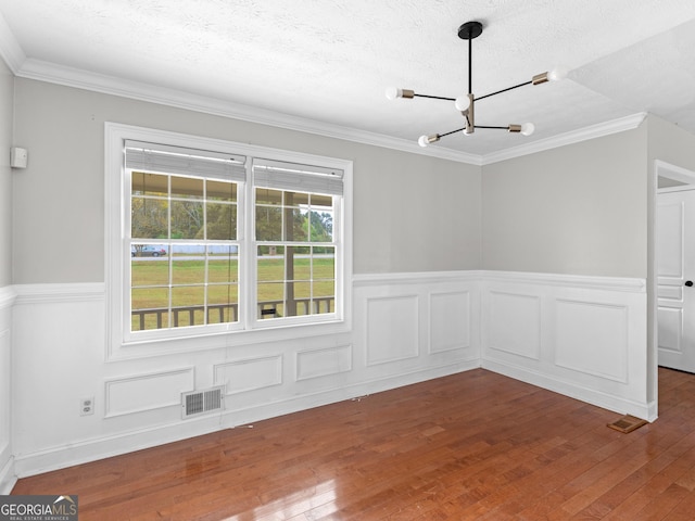 empty room with a textured ceiling, visible vents, a chandelier, and wood finished floors