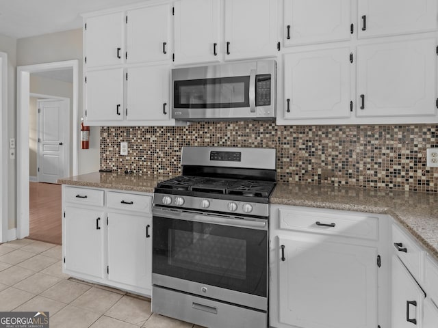 kitchen with white cabinets, light tile patterned floors, stainless steel appliances, and decorative backsplash